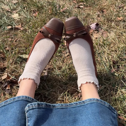 model wearing the bown suede flats with white socks sitting in the grass 